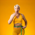 Fitness woman with measure tape isolated on yellow background. Weight loss and healthcare concept