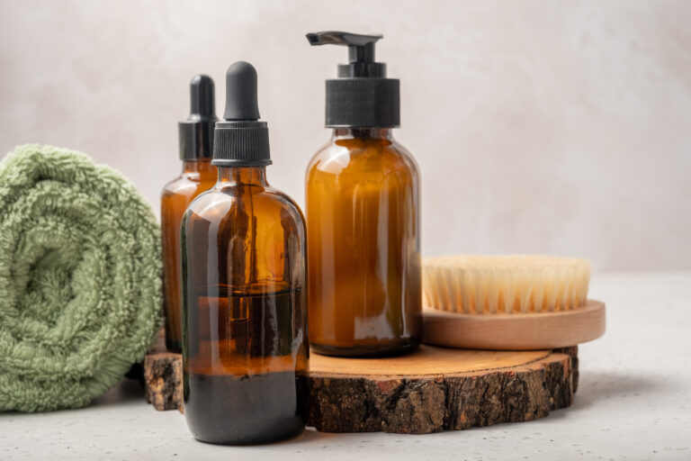 Bottles of dark amber glass with essential oil, massage brush and tropical leaves