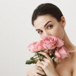 sensual-girlfriend-smelling-bouquet-roses-while-standing-naked-grey_176420-20688