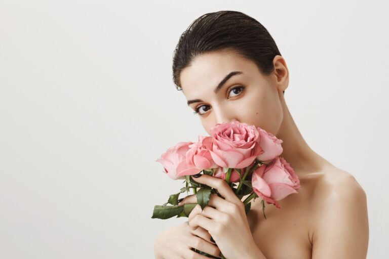 sensual-girlfriend-smelling-bouquet-roses-while-standing-naked-grey_176420-20688