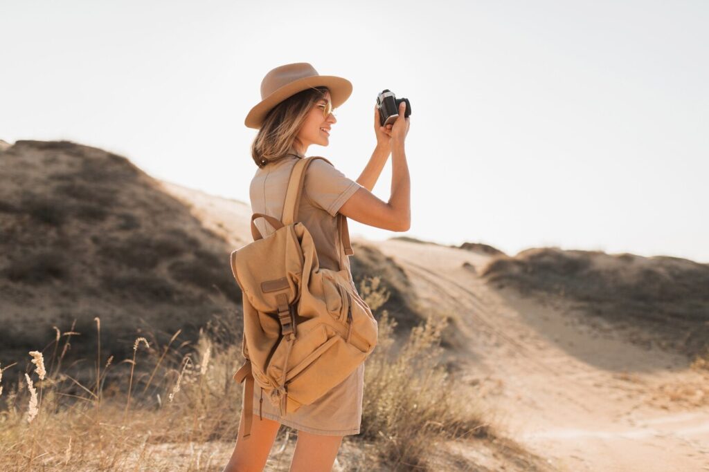attractive-stylish-young-woman-khaki-dress-desert-traveling-africa-safari-wearing-hat-backpack-taking-photo-vintage-camera_285396-9174